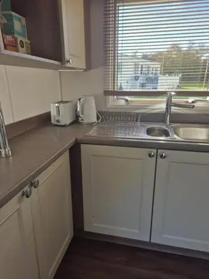 a kitchen with white cabinets and a sink and a window at Lovely Caravan With Front Decking At Carlton Meres Park Ref 60018R in Saxmundham