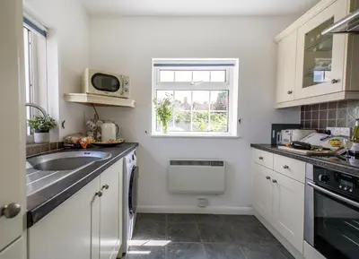 a white kitchen with a sink and a window at Quayside Cottage in Waldringfield
