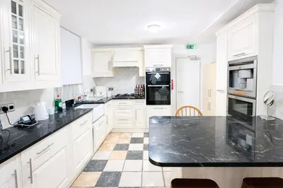 a kitchen with white cabinets and black counter tops at landvue stays, The Colchester town White House 4 bed 2 bath! in Mundon