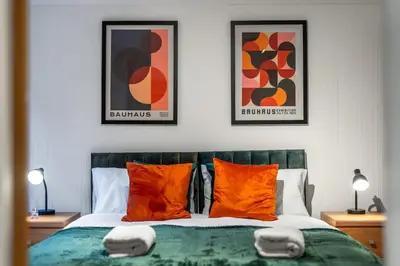 a bedroom with a bed with orange pillows and posters at Bishops Stortford 2 Bed Flat - Free Parking - STN in Bishops Stortford