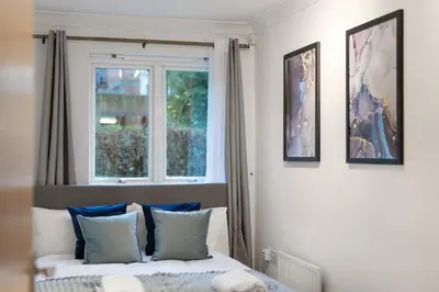 a bedroom with a bed with blue pillows and a window at Bishops Stortford 2 Bed Flat - Free Parking - STN in Bishops Stortford