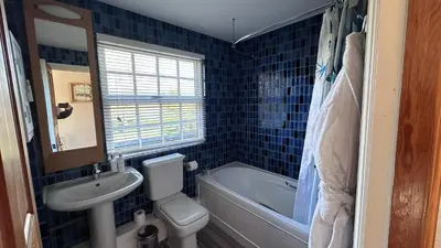 a blue tiled bathroom with a toilet and a sink at The Coach House WPH, Epping in Epping