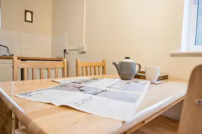 a table with a newspaper and a tea kettle on it at 1 Hall Farm Cottage, Aldeburgh in Aldeburgh