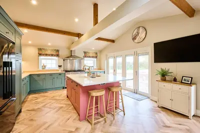 a kitchen with green cabinets and a tv on the wall at Host & Stay The Coral Cottage in Wymondham