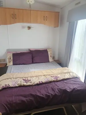 a bedroom with a bed with purple sheets and a window at Hutleys Caravan Holiday Home - St Osyth - Clacton-on-Sea in Saint Osyth