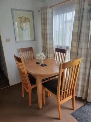 a wooden table with three chairs and a vase with flowers at Hutleys Caravan Holiday Home - St Osyth - Clacton-on-Sea in Saint Osyth