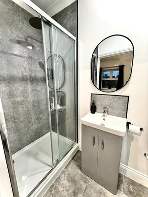 a bathroom with a shower and a sink and a mirror at Sleep Hub in Leiston