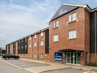 a large brick building with a car parked in a parking lot at Travelodge Stansted Great Dunmow in Great Dunmow
