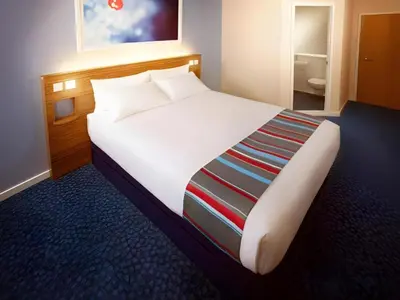 a large white bed in a room with a bathroom at Travelodge Haverhill in Haverhill