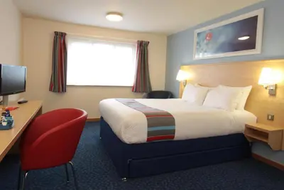 a hotel room with a bed and a desk and a television at Travelodge Ipswich Beacon Hill in Needham Market