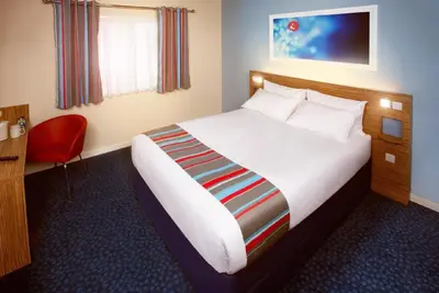 a hotel room with a bed and a red chair at Travelodge Ipswich Capel St Mary in Capel Saint Mary