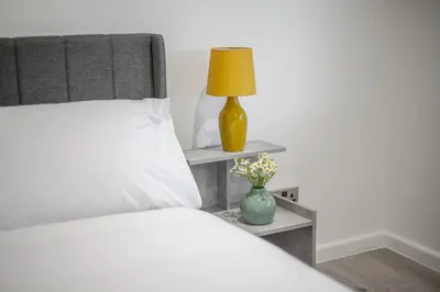 a bed with a yellow lamp and a vase with flowers at Chic & Cosy 2 Bed Maisonette with Freeparking near Chelmsford City Centre in Chelmsford