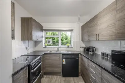 a kitchen with wooden cabinets and a black dishwasher at Chic & Cosy 2 Bed Maisonette with Freeparking near Chelmsford City Centre in Chelmsford