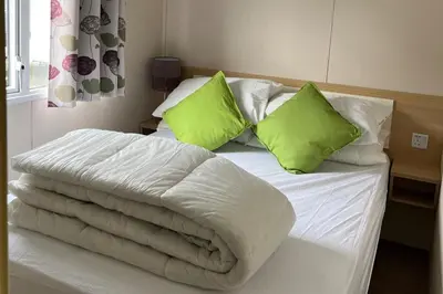 a bed with white sheets and green pillows at Cabin - Sleeps 6 - Beach 10 minutes drive in Clacton-on-Sea