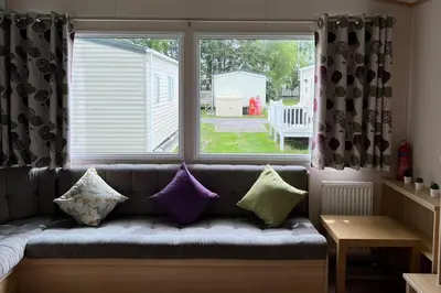a couch with pillows sitting in front of a window at Cabin - Sleeps 6 - Beach 10 minutes drive in Clacton-on-Sea