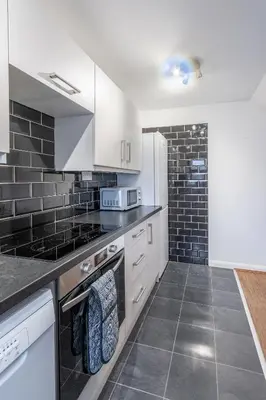 a kitchen with white cabinets and black tiles at A lovely modern comfortable one bedroom house - Pass the Keys in Southend-on-Sea