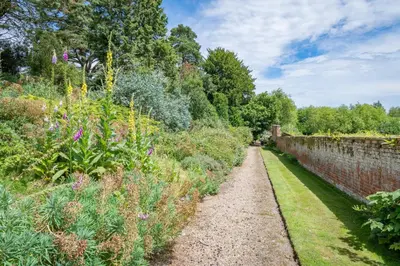 a garden with flowers and a brick wall at Gardeners Cottage by Group Retreats in Hadleigh