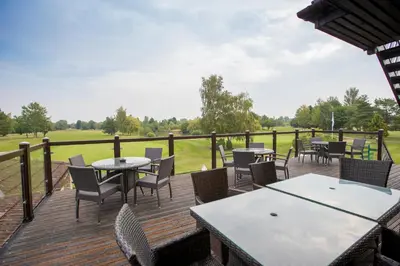 a deck with tables and chairs on a golf course at Lakeside Lodge Golf and Country Club in Huntingdon