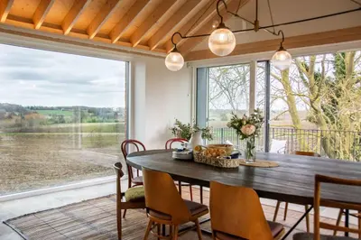 a dining room with a table and chairs and a large window at The Barn at Manor Farm in Great Glemham