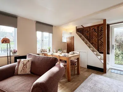 a living room with a table and chairs and a staircase at Columbine Cottage by The Suffolk Cottage Collection in Middleton