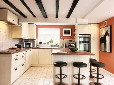 a kitchen with white cabinets and black bar stools at Peak Hill Cottage in Theberton