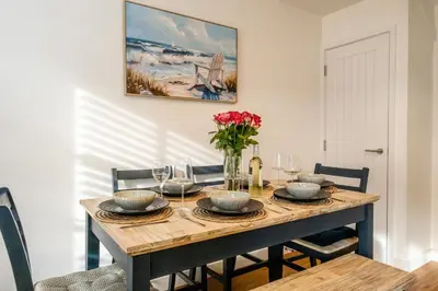 a dining room table with glasses and a vase of flowers at 4 Oakes Court, Thorpeness - Sleeps 6 - Close to Thorpeness Meare and the beach, Close to Thorpeness Golf, Hotel and Country Club, Only 2 miles from #Aldeburgh, Managed by Aldeburgh Coastal Cottages in Thorpeness