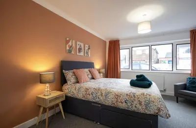 a bedroom with a bed and a chair and windows at Shrub End Lodge - Colchester in Lexden