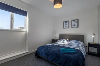 a bedroom with a bed with a blue blanket and a window at Sizewell - Lincoln - Contractor Accommodation in Saxmundham