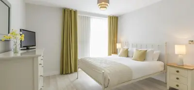 a white bedroom with a bed and a television at Citystay Living - Vesta Apartments in Cambridge