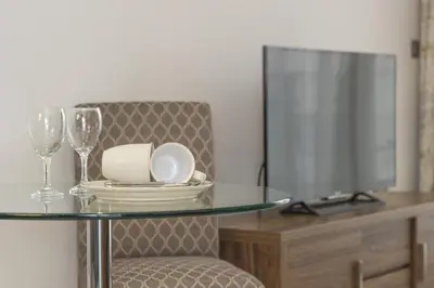 a glass table with plates and wine glasses and a television at Citystay Living - Vesta Apartments in Cambridge