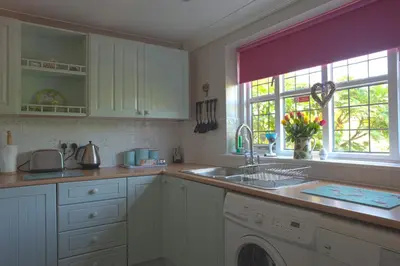 a kitchen with white cabinets and a sink and a window at Little Chequers in Friston