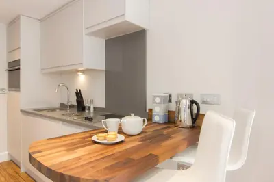 a kitchen with a wooden table and white cabinets at Citystay Living - The Dales in Cambridge