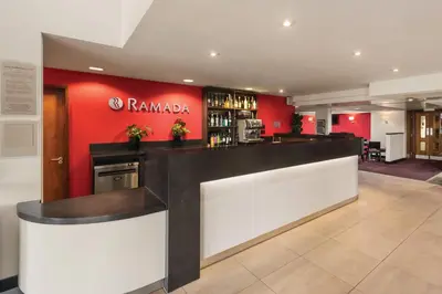 a bar in a restaurant with a red wall at Ramada Cambridge in Cambridge