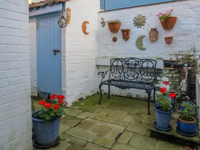 a bench in a courtyard with potted plants and a blue door at Ivy Cottage in Aldeburgh