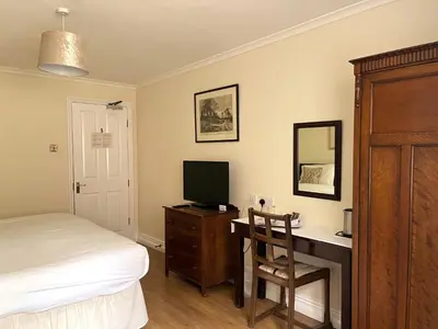 a bedroom with a bed and a desk with a television at The Cottage Guest House in Bishops Stortford