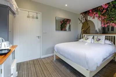 a bedroom with a bed with white sheets and flowers on the wall at The Bell Inn in Newmarket