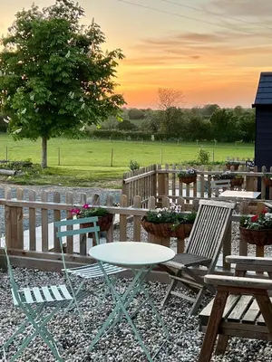 a group of tables and chairs with a sunset in the background at Great Sampford B&B Sorrells farm in Hempstead