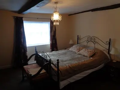 a bedroom with a bed and a window and a chandelier at Minsmere Cottage in Yoxford