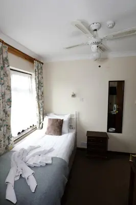 a bedroom with a bed with white sheets and a ceiling fan at Aylesbray Lodge in Cambridge