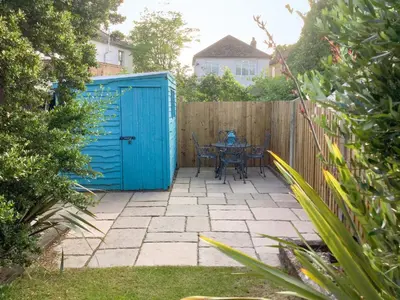 a patio with a blue shed and a table at Sea Folly in Brightlingsea