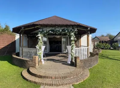 a gazebo with an arch and chairs in a yard at Rettendon Lodge in Battlesbridge