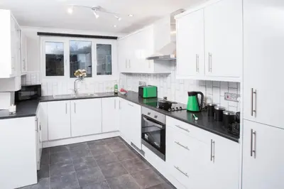 a white kitchen with white cabinets and black counter tops at Wherstead House in Ipswich