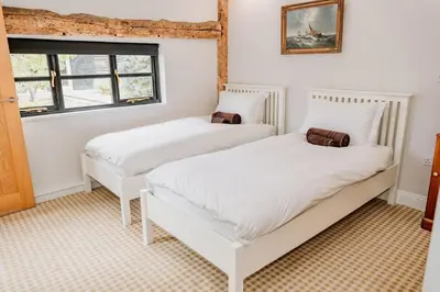 two white beds in a room with two windows at Creeksea Place Barns in Burnham on Crouch