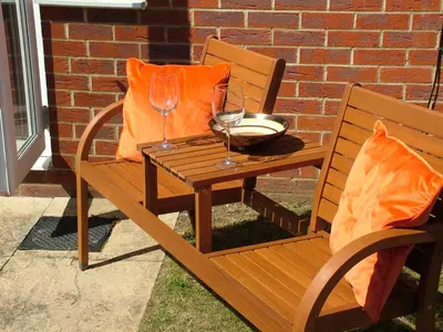 a wooden bench with a table and two wine glasses at Thistle Cottage in Mildenhall