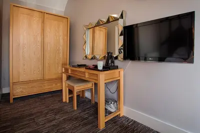 a hotel room with a desk and a television on a wall at The Saracens Head Hotel - The Coaching Inn Group in Great Dunmow