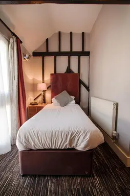 a bedroom with a large bed with a wooden headboard at The Saracens Head Hotel - The Coaching Inn Group in Great Dunmow