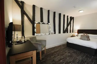 a hotel room with a bed and a desk and a mirror at The Saracens Head Hotel - The Coaching Inn Group in Great Dunmow