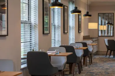 a dining room with tables and chairs and windows at Cambridge Belfry Hotel & Spa in Cambridge