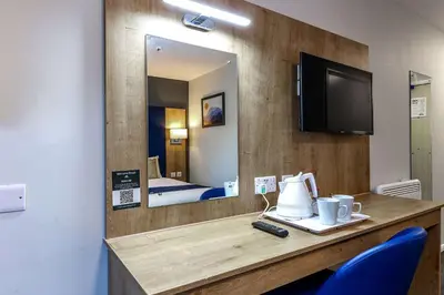 a hotel room with a desk and a mirror at Days Inn London Stansted Airport in Stansted Mountfitchet