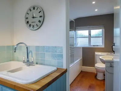 a bathroom with a clock on the wall and a sink at Thimble Cottage - Aldeburgh Coastal Cottages in Aldeburgh